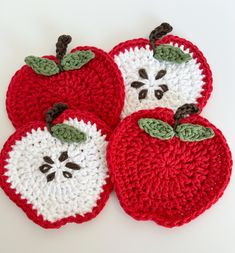 three crocheted apples are sitting on a white surface, one is red and the other has green leaves