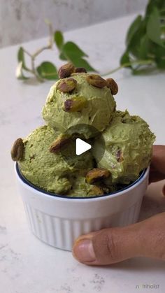 a hand holding a bowl filled with green ice cream and pistachio nuts on top