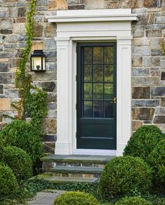 a black front door and steps leading up to the house with green bushes around it