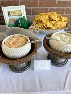 two bowls filled with dips and chips on top of a white tablecloth covered table