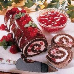 a cake roll with strawberries and raspberries on it next to a bowl of cherries