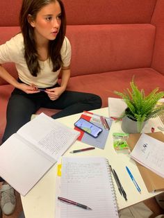 a woman sitting on the floor in front of a table with notebooks and pens