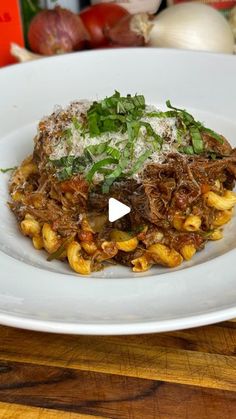 a white plate topped with pasta and meat covered in sauce on top of a wooden table