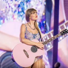 a woman holding a pink guitar on stage