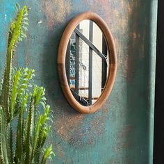 a round mirror mounted to the side of a green wall next to a potted plant