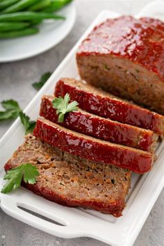 slices of meatloaf on a white platter with green beans and parsley