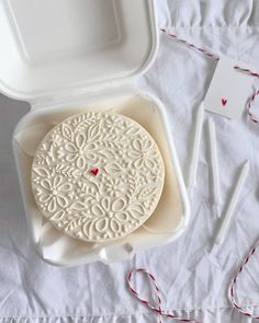 a white box with a red heart on it next to some knitting needles and thread