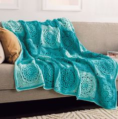 a green crocheted afghan sits on a couch in front of two framed pictures