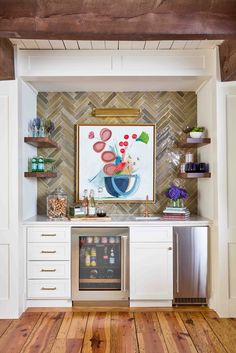 a kitchen with wood floors and white cabinets, an art piece on the wall above the refrigerator