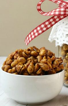 a white bowl filled with nuts next to a jar of candies and a red checkered ribbon