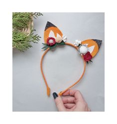 a hand holding an orange cat ears headband with flowers and leaves on the top