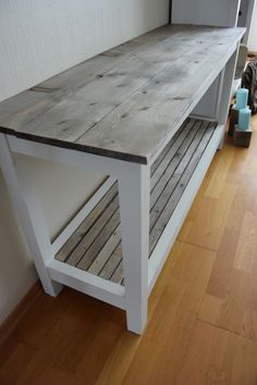 a wooden bench sitting on top of a hard wood floor next to a wall and window