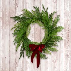 a green wreath with red ribbon hanging on a white wooden wall and wood planks