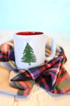 a white cup with a green christmas tree on it sitting on top of a plaid napkin