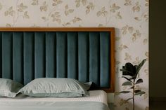 a bed with a blue headboard and pillows on it next to a flowered wallpaper