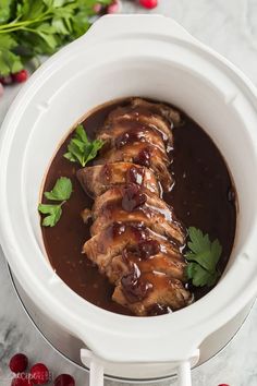 a white crock pot filled with meat covered in sauce and garnished with parsley