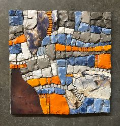 a piece of art made out of rocks and orange, blue and white tiles on a gray surface