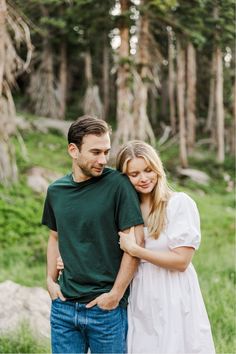 a man and woman standing next to each other in front of some trees with their arms around each other