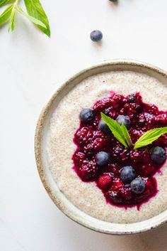 a bowl of oatmeal with blueberries and mint leaves on the side