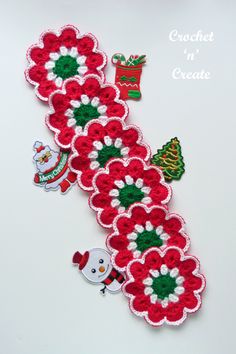 a crocheted christmas decoration with red flowers and green leaves on the side, sitting on a white surface