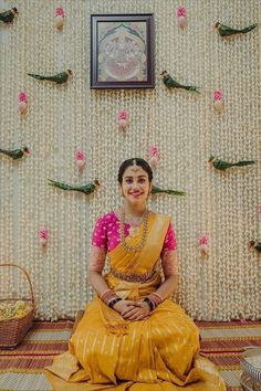 a woman sitting on the floor in front of a wall with flowers and birds hanging from it