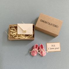 a pair of pink baby shoes sitting next to a box with congratulations written on it