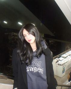 a woman with long black hair standing in front of an escalator and looking at the camera