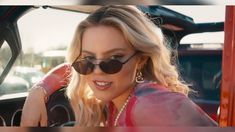 a blonde woman wearing sunglasses sitting in the driver's seat of a car