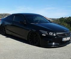 a black car parked on the side of a road near some hills and trees in the background