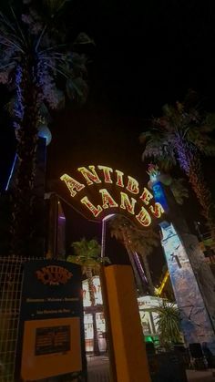 the entrance to an amusement park at night with palm trees and neon signs on it