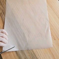 a person in white gloves is cutting paper on a wooden table with scissors and a knife