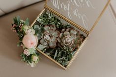 two wedding rings are placed in a box with succulents and greenery