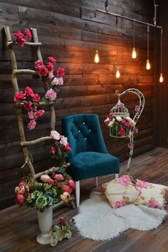 a blue chair sitting in front of a wooden wall with flowers on it and a birdcage hanging from the ceiling