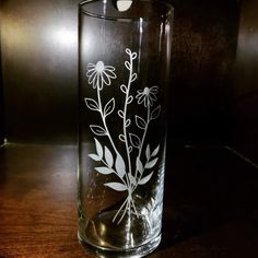 a glass vase with flowers etched on the side sitting on a wooden countertop in front of a dark background