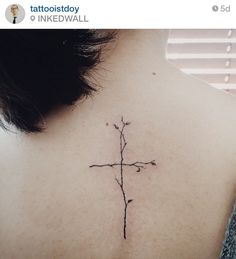 a cross tattoo on the back of a woman's upper back neck, with small flowers growing out of it