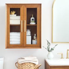 a bathroom cabinet with towels and soaps in it next to a sink, toilet and mirror