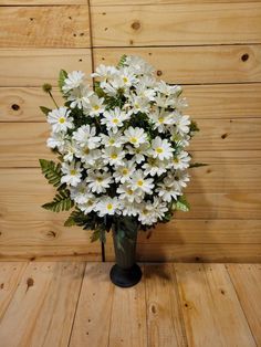 a vase filled with lots of white flowers on top of a wooden table next to a wall