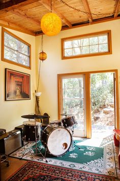 a drum set sits in the middle of a room with two windows and a rug on the floor