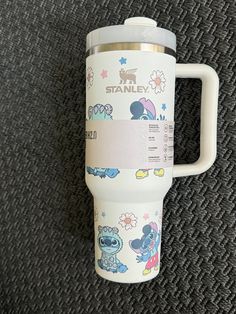 an insulated travel mug with cartoon characters on it sitting on a carpeted surface