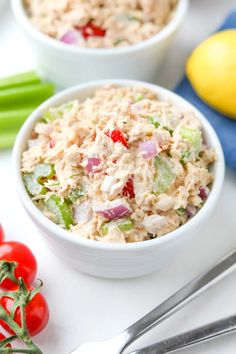 two bowls filled with tuna salad on top of a white table next to lemons and tomatoes