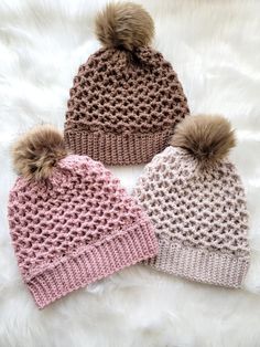 three knit beanies with pom - poms on top, one in pink and the other in brown