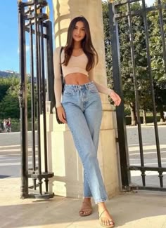 a woman standing next to a gate wearing high waist jeans and a cropped top