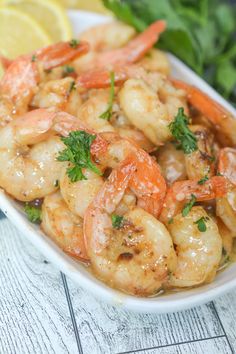 a white bowl filled with cooked shrimp and garnished with parsley next to lemon wedges