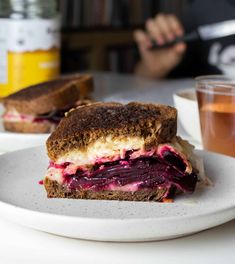 there is a sandwich on a white plate next to a cup of tea and a drink