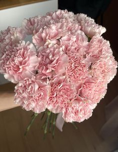 a bouquet of pink carnations in a vase on a wooden table next to a mirror