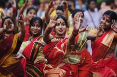 women in red and yellow sari dance with their hands up to the sky while others look on