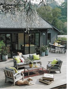 a dog laying on top of a wooden deck next to chairs and tables with yellow pillows