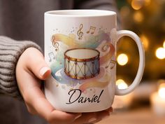 a person holding a coffee mug with musical notes on it and a drum in the middle