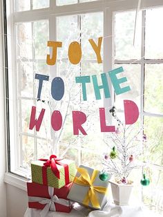 christmas presents are piled up in front of a window with the words joy to the world on it