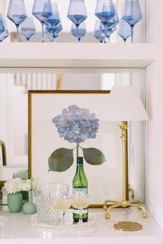 there is a vase with blue flowers in it on the table next to glasses and a lamp